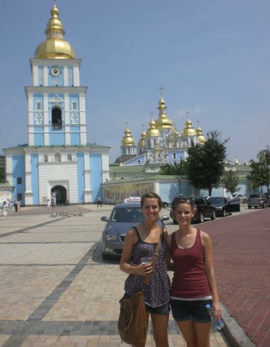 Young woman stands smiling outside with friend in front of buildings in Ukraine