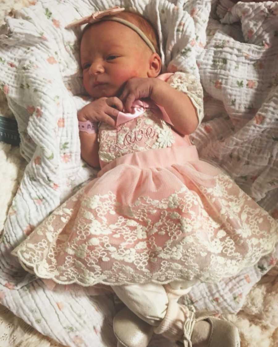 Newborn girl lays on her back in fancy pink dress with white detailing