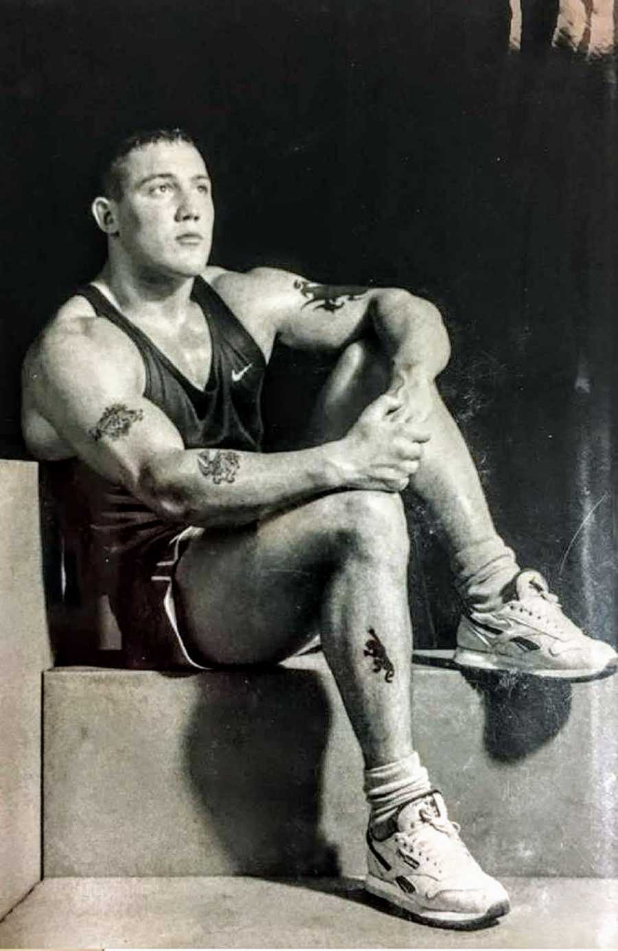 Muscular man sits posing on step with tattoos on arms and legs