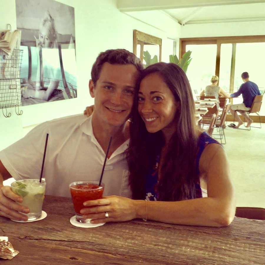 Husband and wife sit at bar smiling with arms around each other