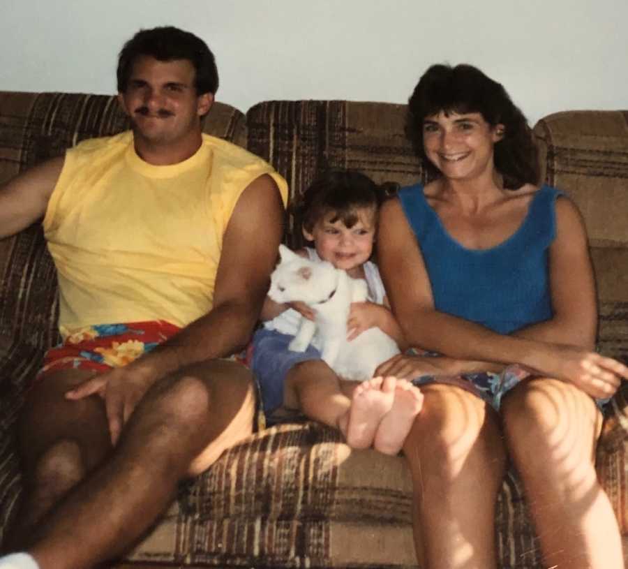 Little girl sits on couch with cat in her lap with her mother and father beside her who are now divorced