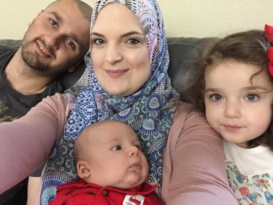 Woman who converted to Islam sits on couch smiling with husband and two kids in selfie