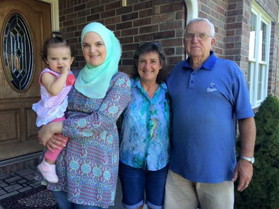 Woman who converted to Islam stands outside home holding daughter as she stands beside her parents