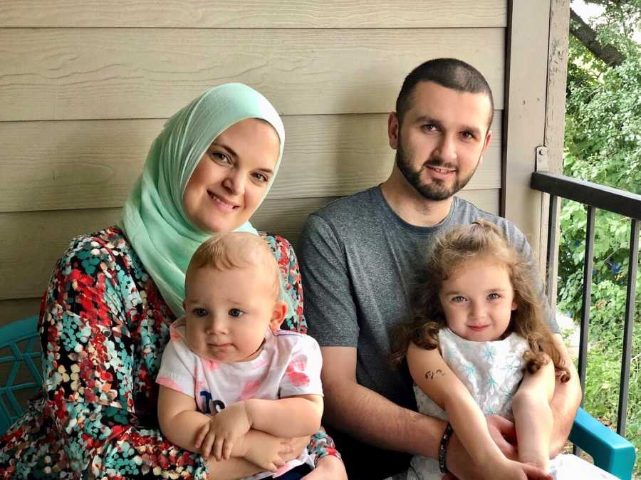 Husband and wife sit on porch with their son and daughter in their laps