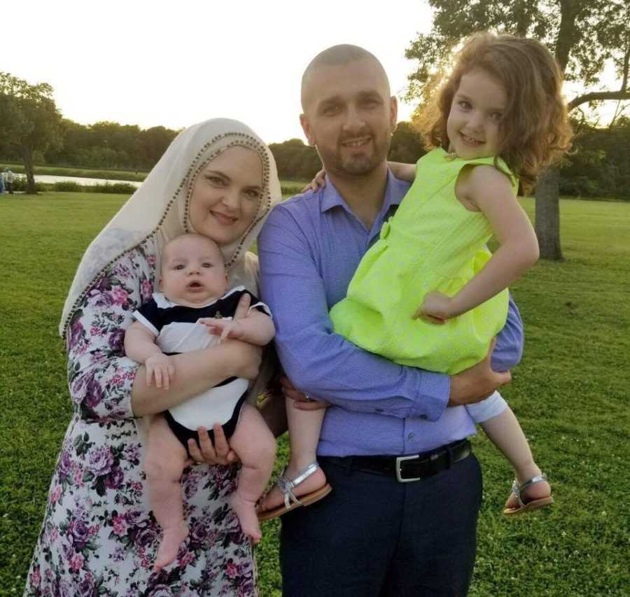 Husband and wife stand outside holding their two children