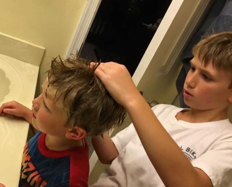 Little boy standing in bathroom searching through little brothers hair who has lice