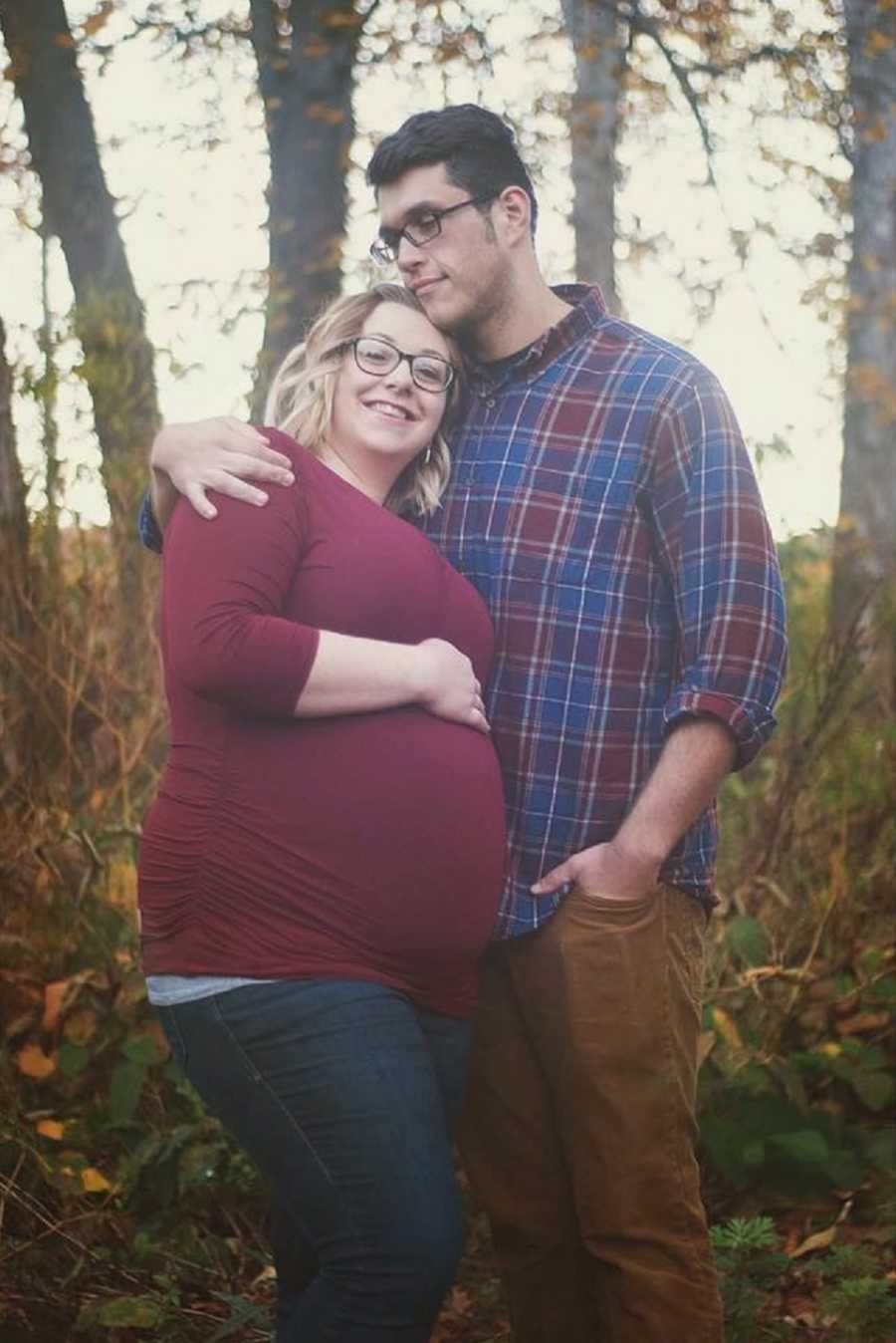 Pregnant woman with eating disorder stands smiling in wooded area with husband