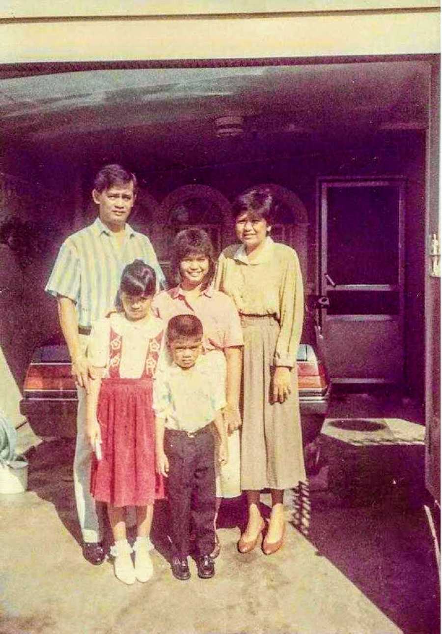 Little girl stands with her brother in front of mother, father, and grandmother