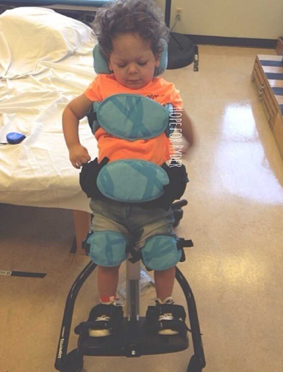 Little boy stands strapped into full body brace in hospital room