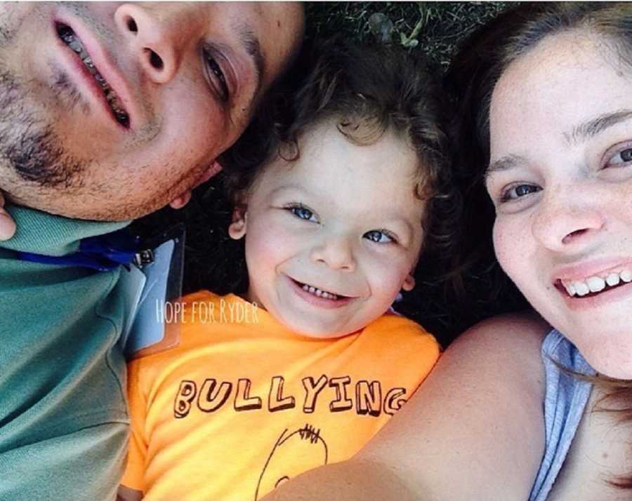 Husband and wife lay on their back on ground with their son with Williams Syndrome between them