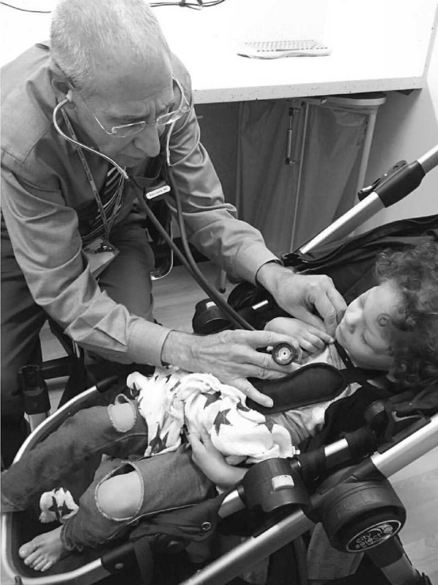 Doctor leans over baby laying in stroller holding stethoscope up to his chest