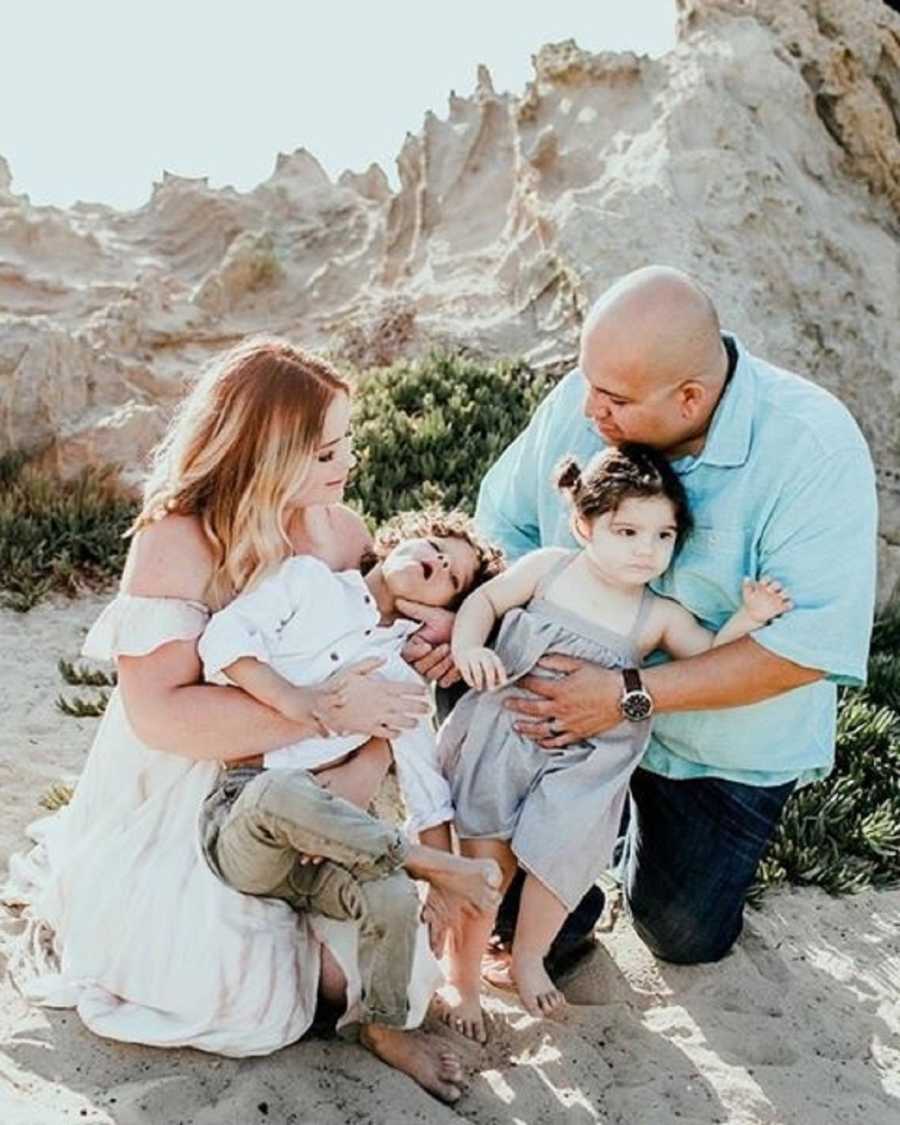 Man and wife kneel on beach with their two young children