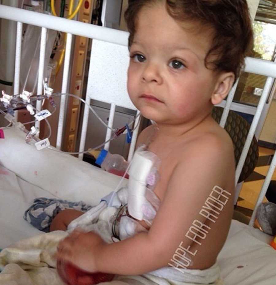 Little boy with Williams Syndrome sits up in hospital crib with bandage on his chest