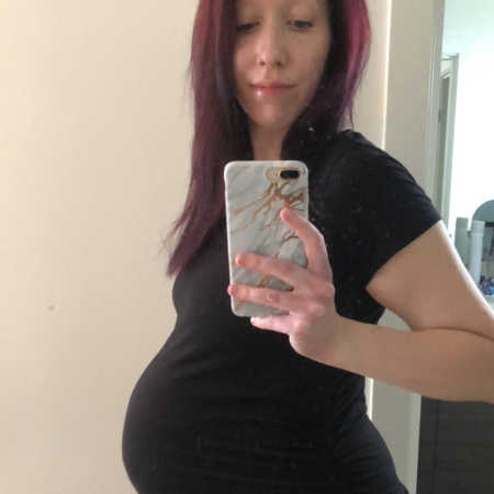 Pregnant woman stands taking mirror selfie with iPhone