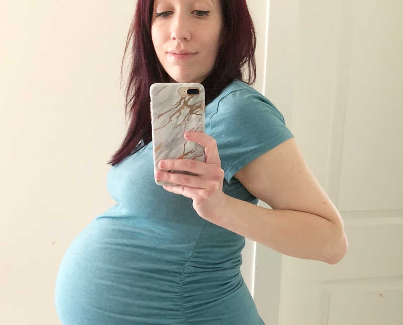 Pregnant woman smiles as she takes mirror selfie with iPhone