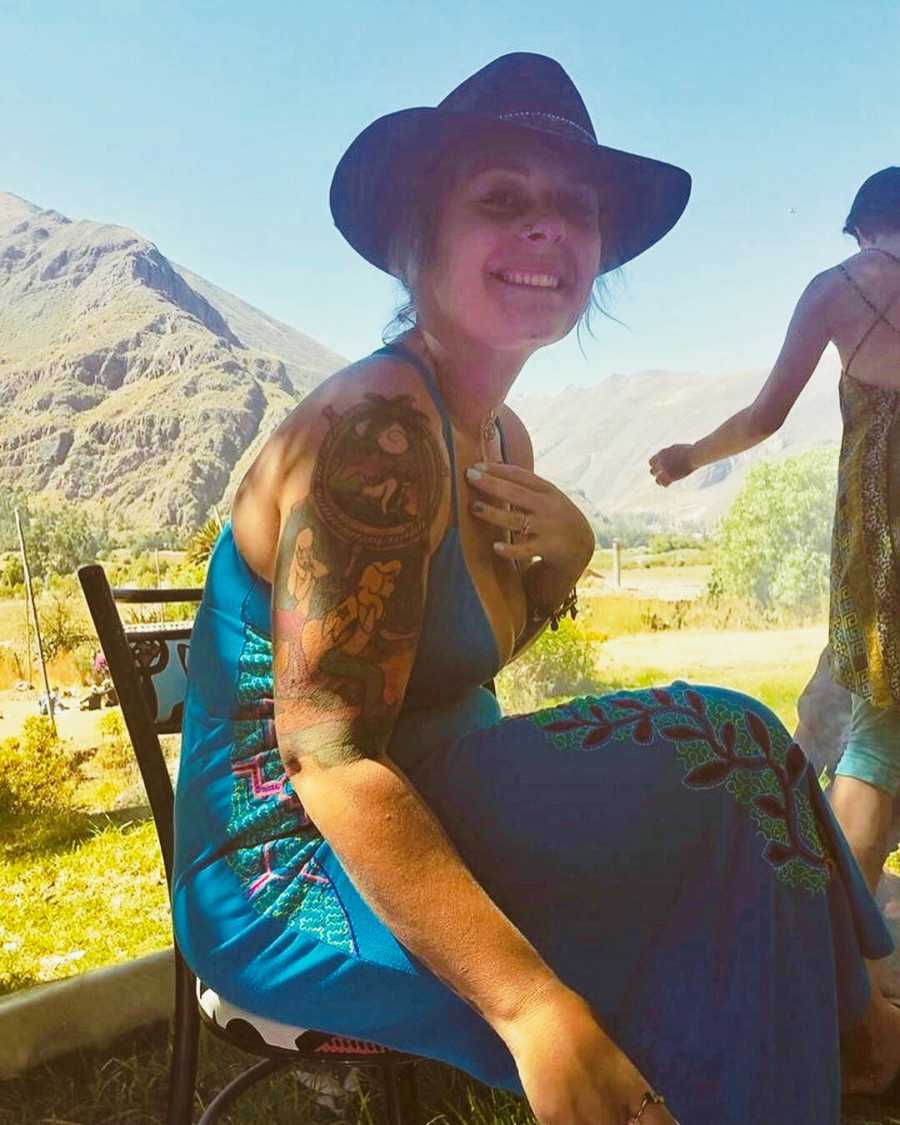 Woman who was kidnapped and abused sits smiling in chair outside with mountains in background