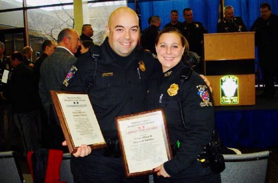 Police man stands smiling beside wife who is also a cop as they hold up certificates