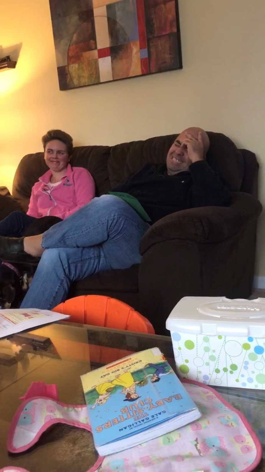 Husband and wife sit on couch in home laughing