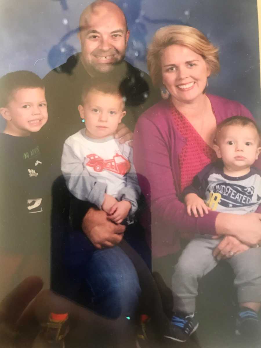 Husband and wife sit smiling with their three sons for family portrait