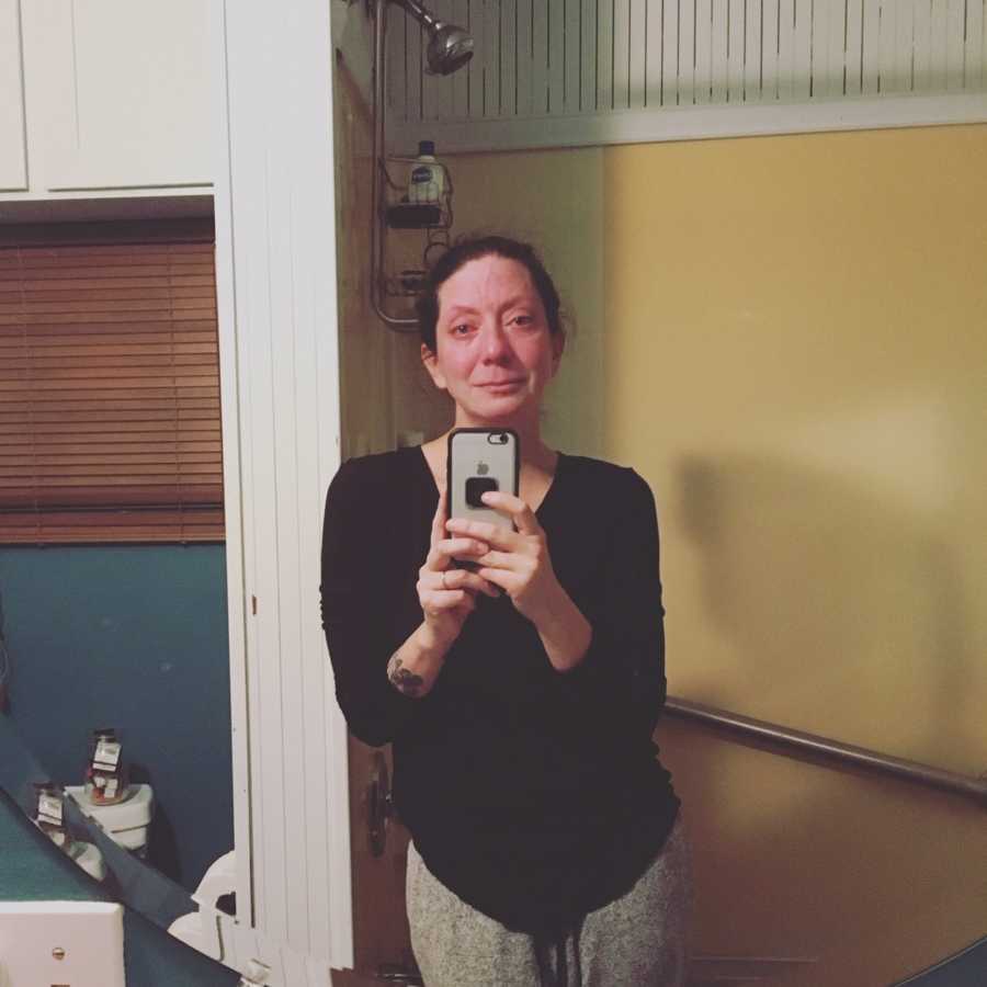 Woman who miscarried stands crying in mirror selfie in bathroom