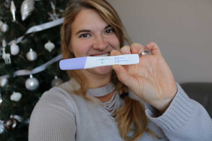 Woman smiles as she holds up positive pregnancy test in front of her face