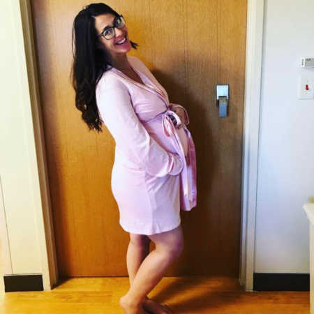Pregnant woman stands smiling in hospital room after battling infertility and going through miscarriage