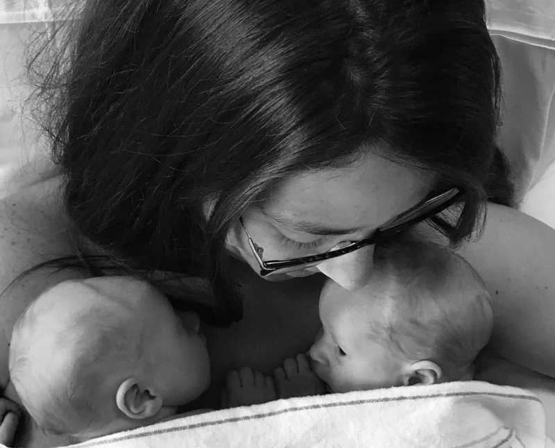 Mother looks down at newborn twins that lay on her bare chest