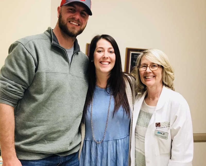 Husband and wife stand smiling with their fertility specialist