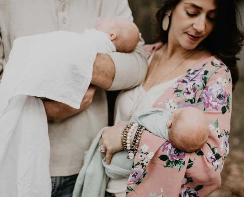 Newborn twins lay asleep in mother and fathers arms