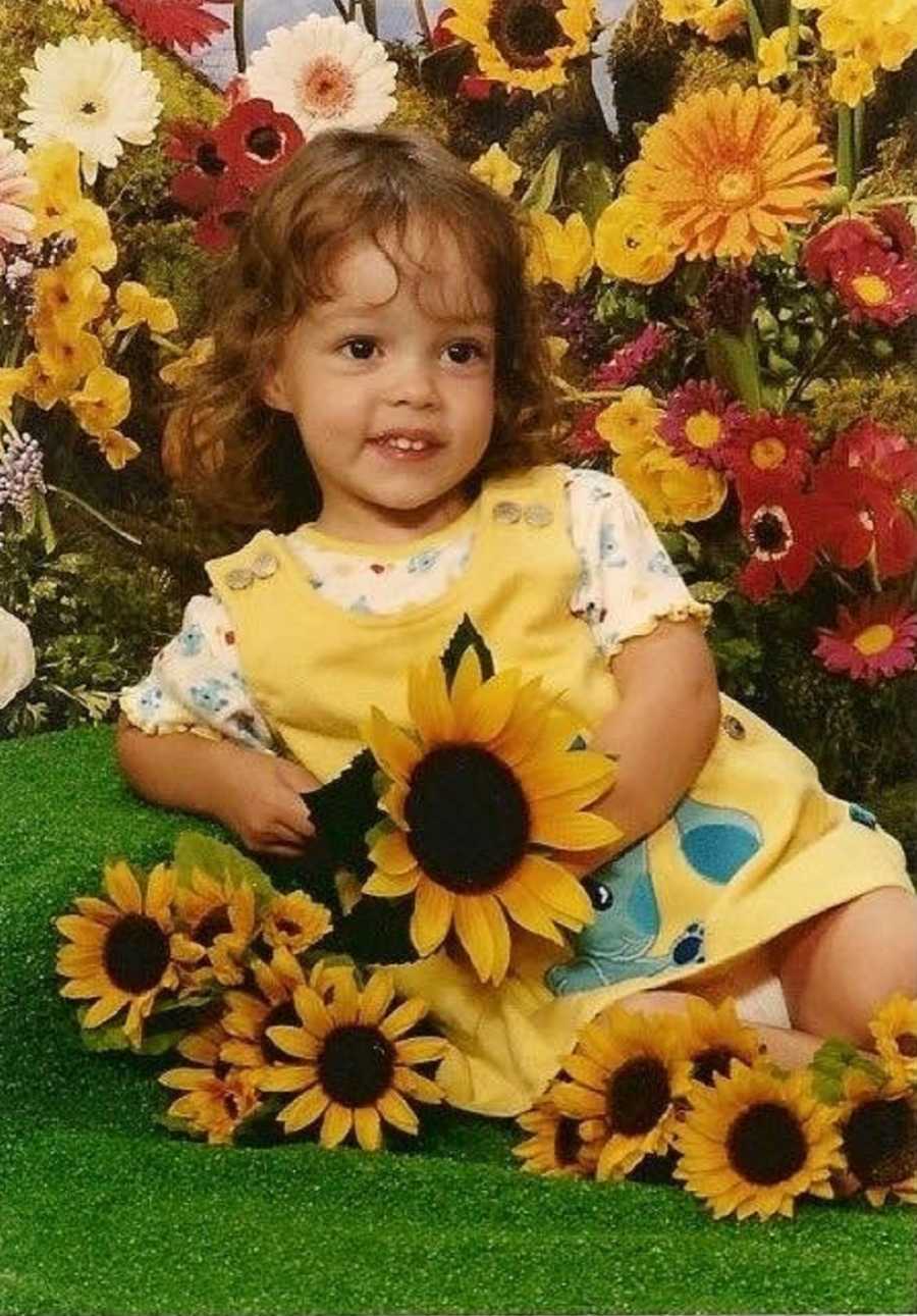 Young girl lays on her side smiling as she holds fake dandelions for photoshoot