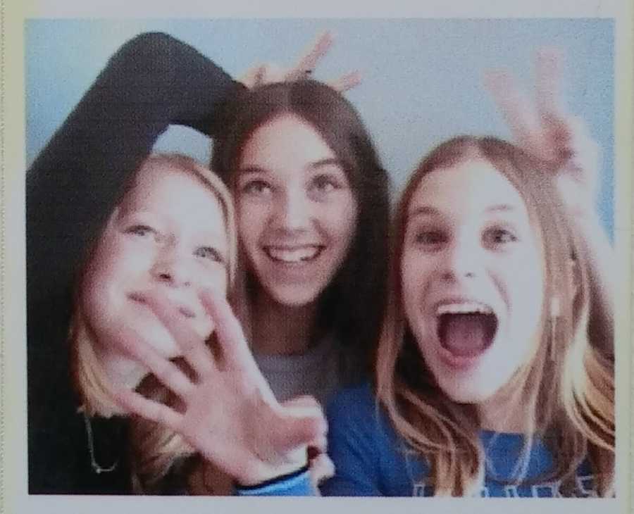 Young girl with POTS smiles in photo booth picture with two friends