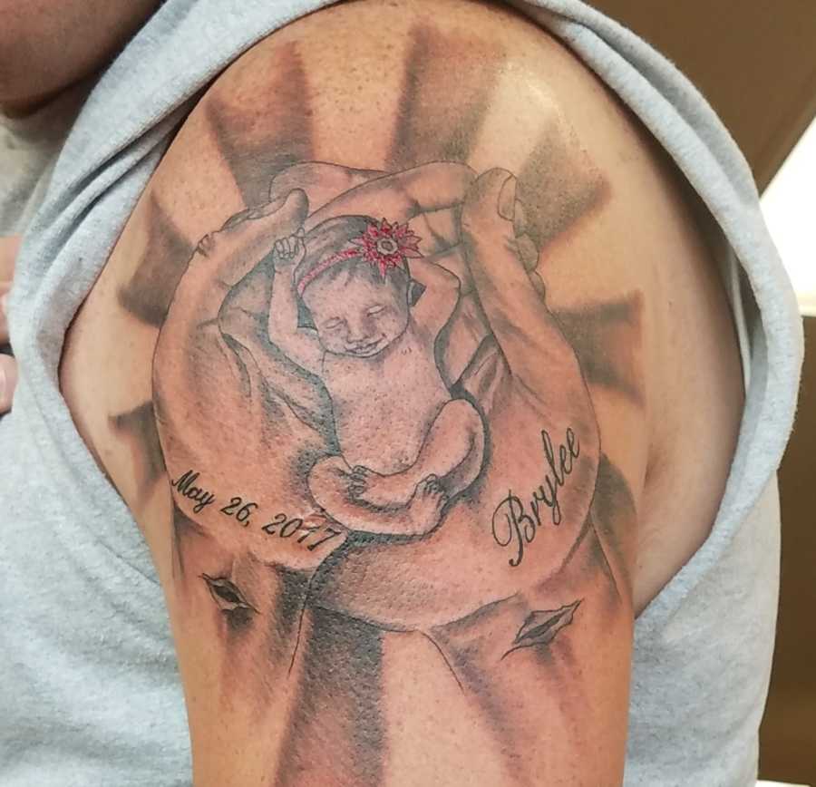 Tattoo on mans's shoulder of hands holding baby girl that is his daughter