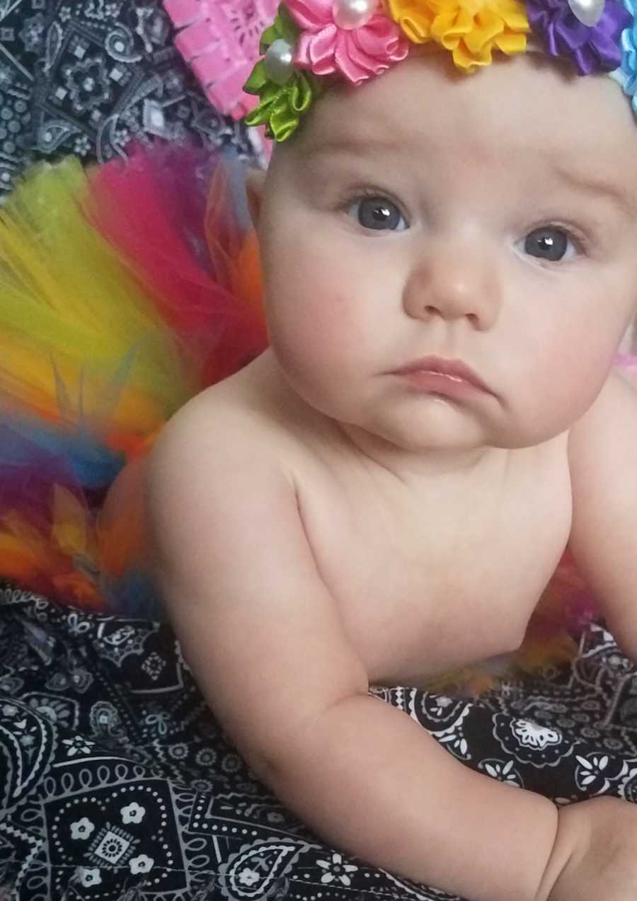 Baby girl lays on stomach wearing flower crown and rainbow tutu