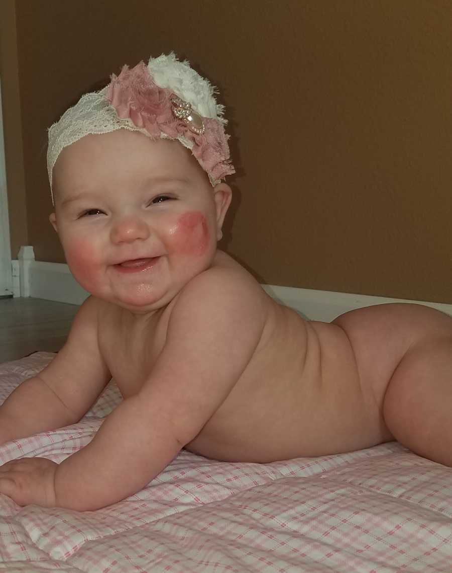 Naked baby girl lays on her stomach smiling with flower headband on