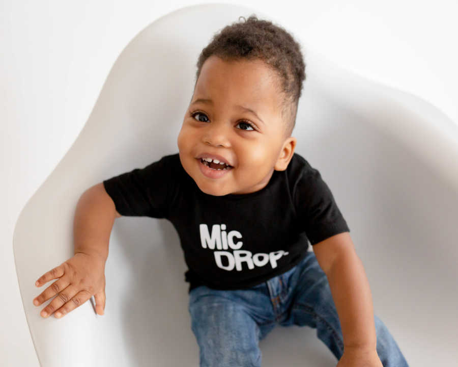 Adopted little boy sits in white chair smiling