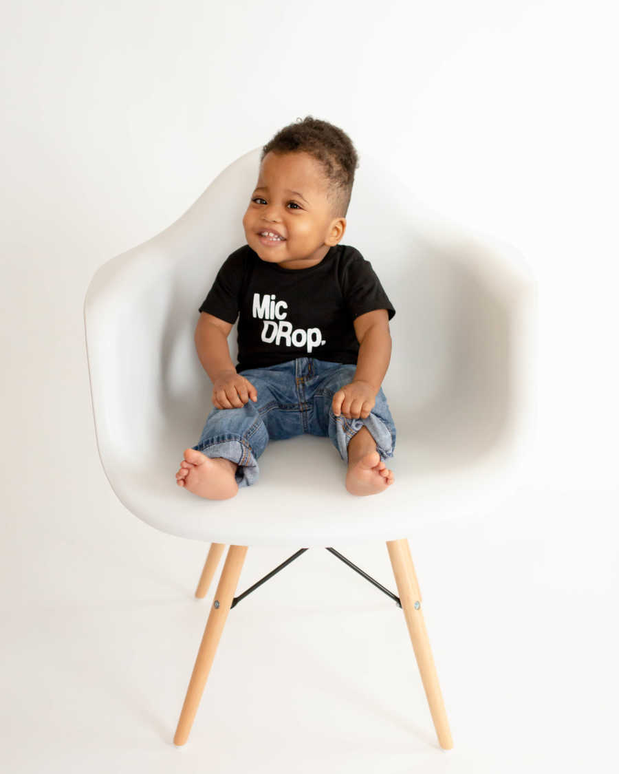 Adopted little boy sits in white chair smiling for photoshoot