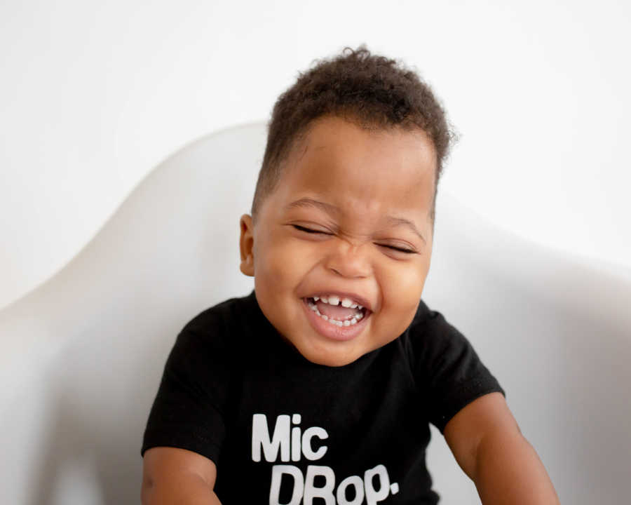 Little boy who was adopted sits in white chair laughing for photoshoot