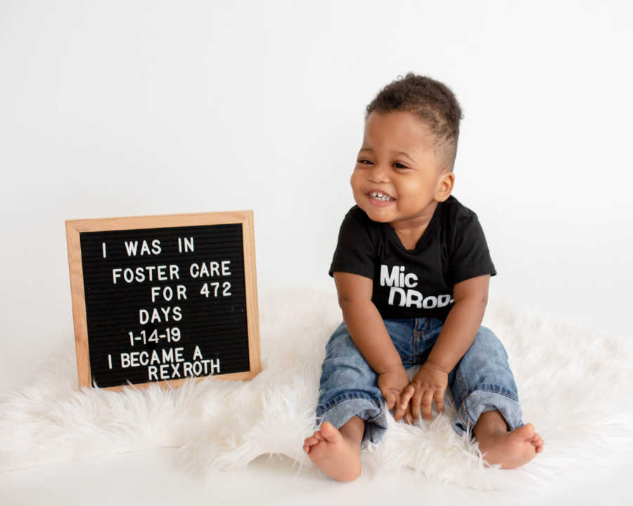 Little boy smiles as he sits next to sign that says, "I was in foster care for 472 days..."