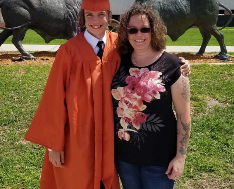 Mother smiles as she stands beside son in orange cap and gown who has ADHD