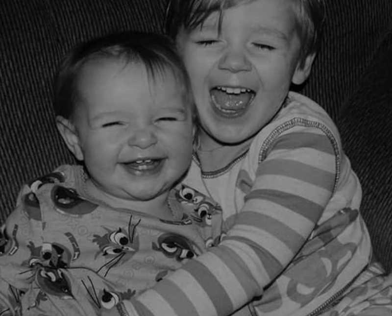 Little boy sits smiling as he wraps his arms around his baby sister