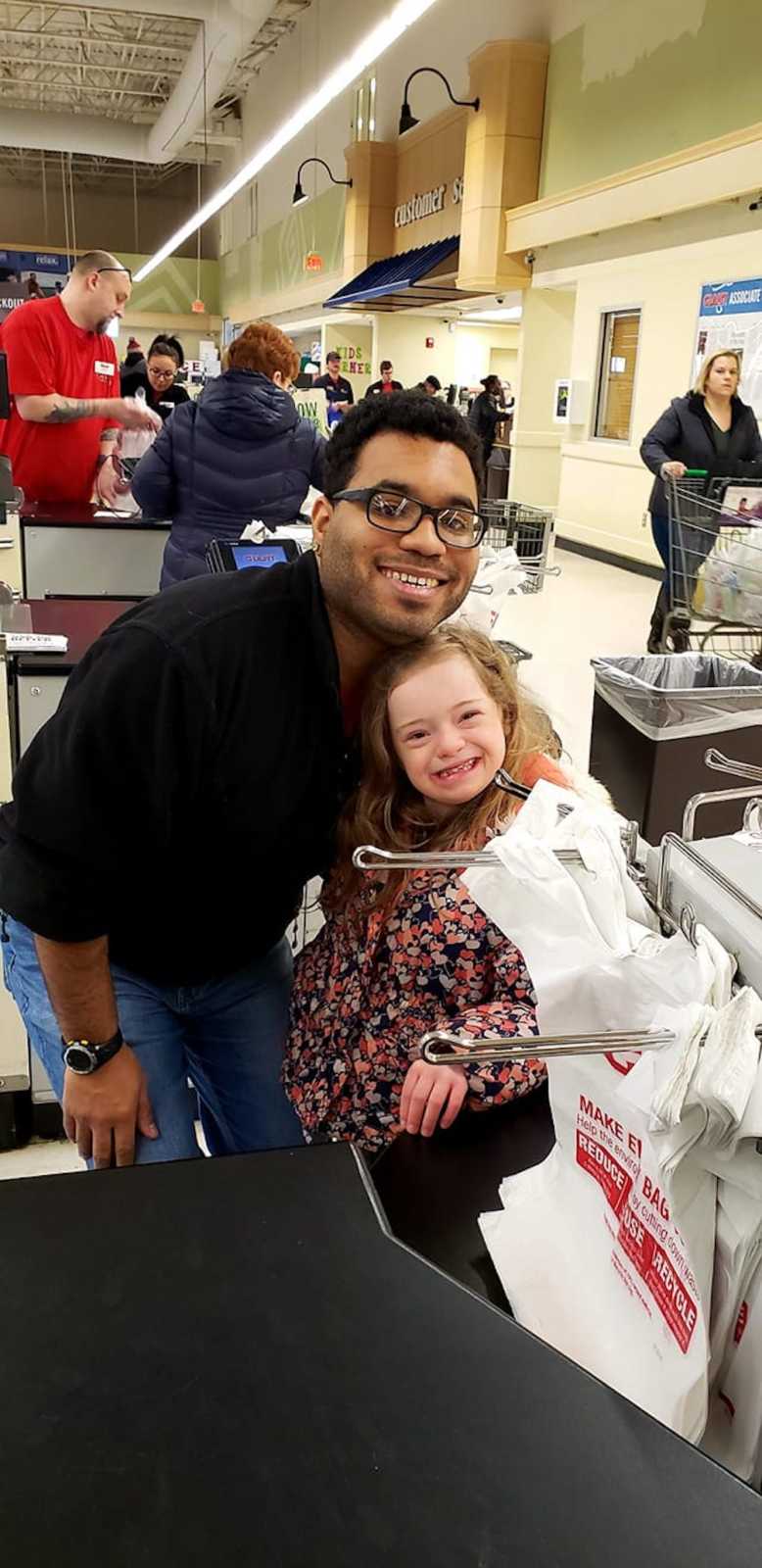 Grocery store worker smiles beside little girl with down syndrome