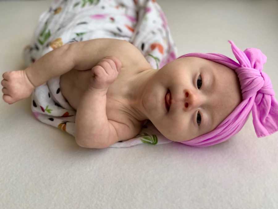 Baby with down syndrome lays swaddled in blanket with pink head wrap on
