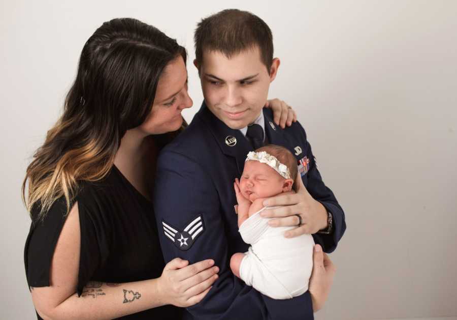 Wife stands beside husband in air force who holds baby girl with Aicardi Syndrome