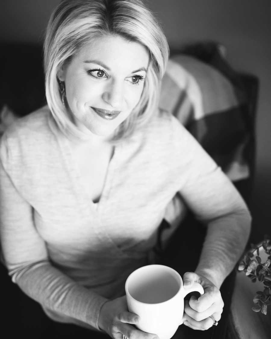 Woman who goes to see a therapist sits at home smiling as she holds coffee mug