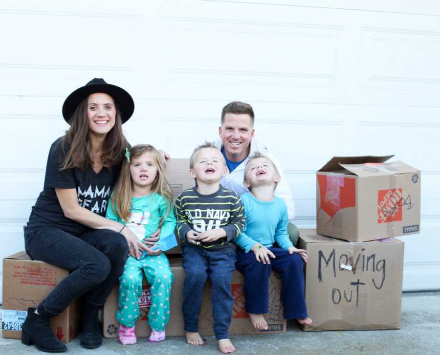 Husband and wife sit on moving boxes in driveway with their triplets 