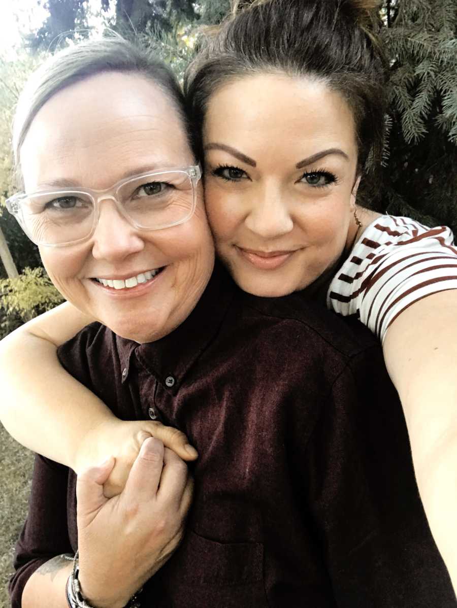 Woman smiles as she takes selfie with arm wrapped around wife
