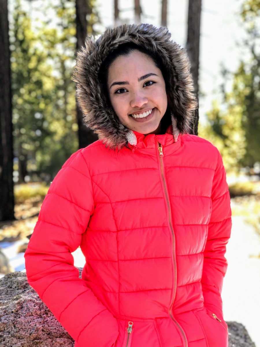 Teen who grew up in predominately white community stands smiling outside wearing winter coat with hood up