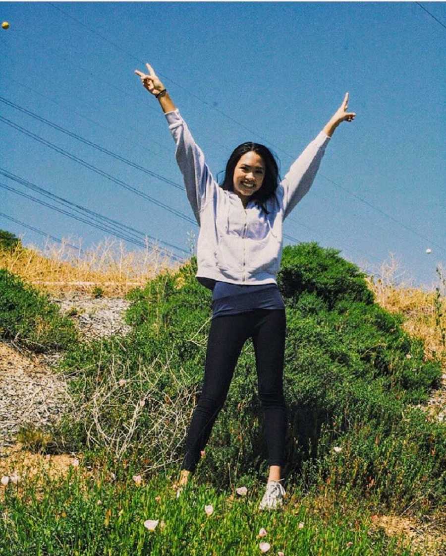 Teen who struggled growing up in predominately white community stands outside holding peace sings in the air