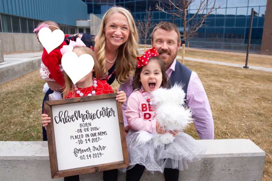 Husband and wife sit outside of adoption court with their three adopted daughters