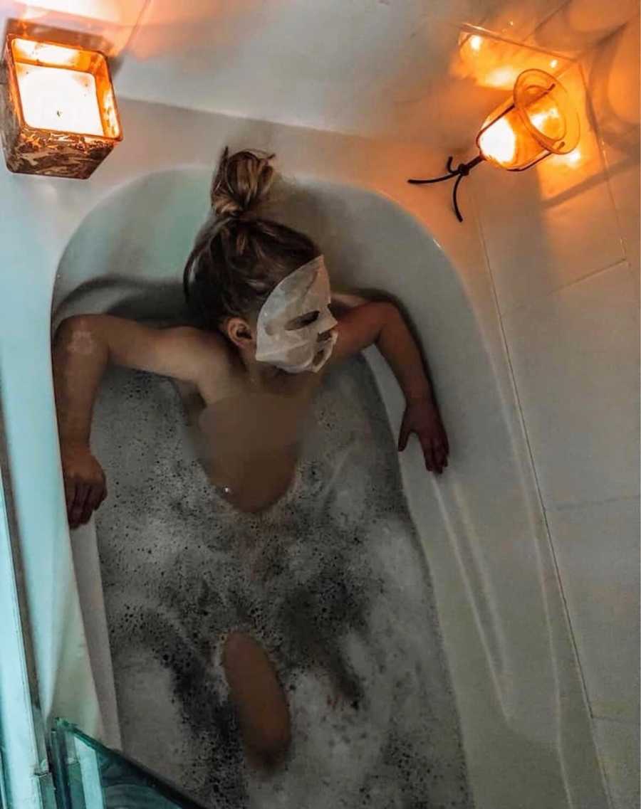 Little girl sits in bathtub with face mask on and candles lit